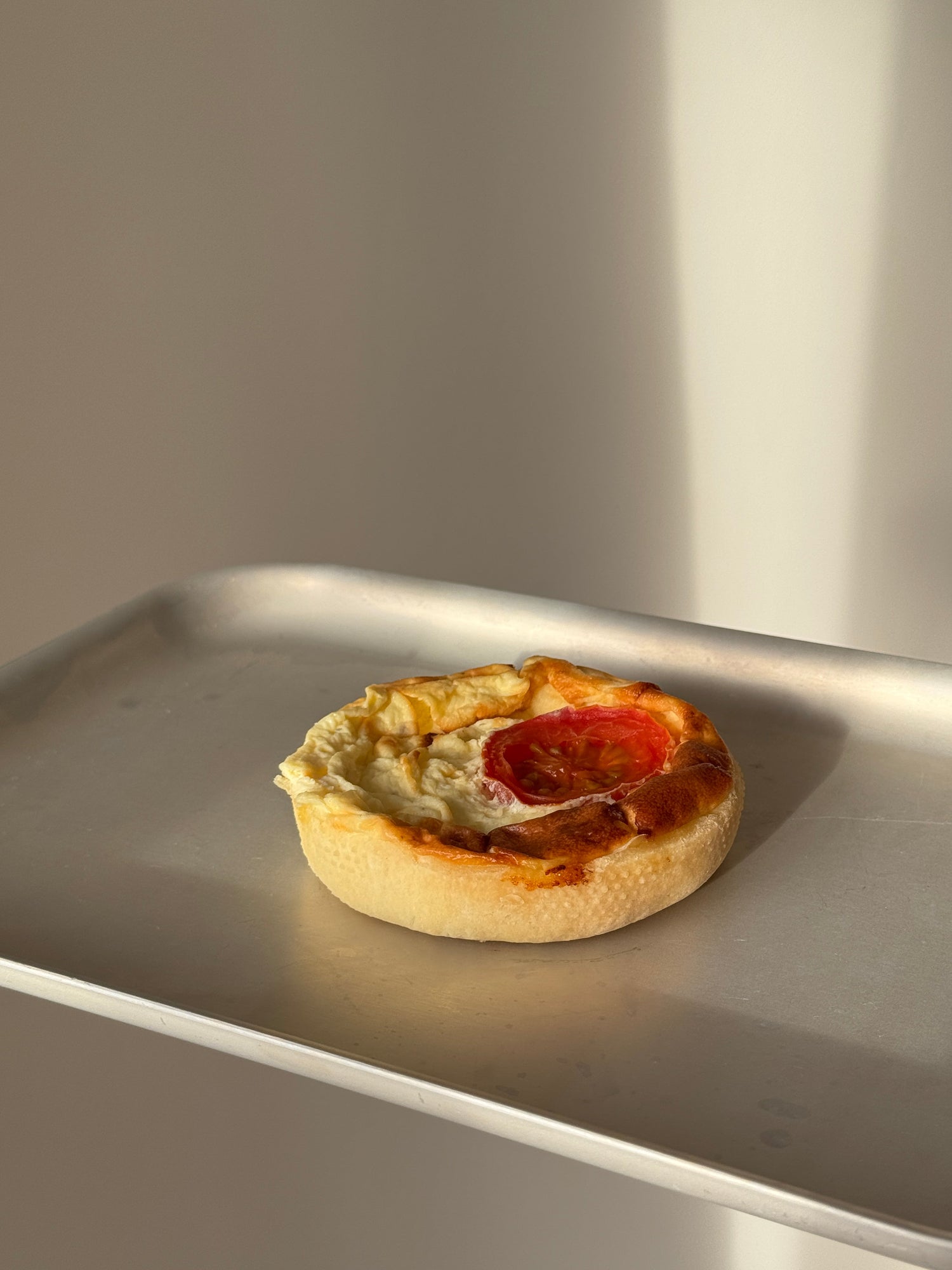 A small round gluten free cheese and tomato quiche taken at an angle on a tray